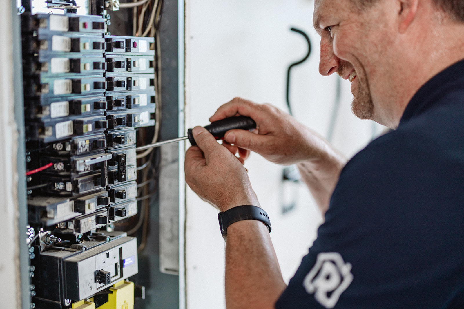 A licensed Randy's electrician smiles while working inside a residential electrical panel.